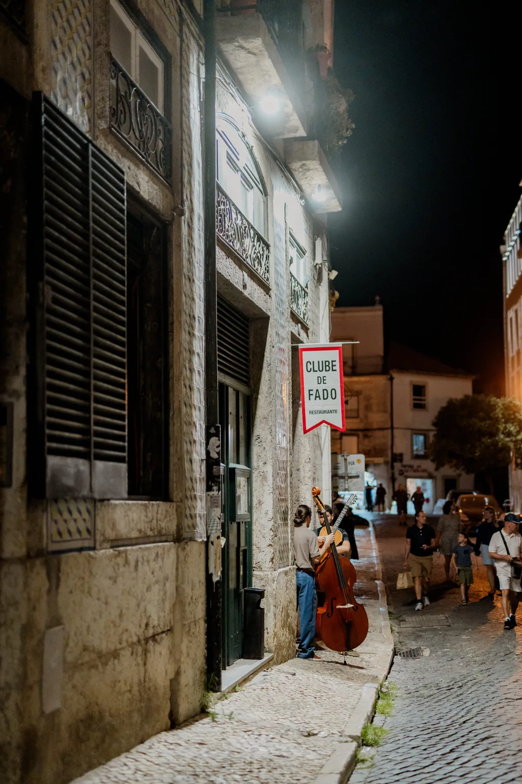 A fachada à noite, com músicos na rua junto à Sé