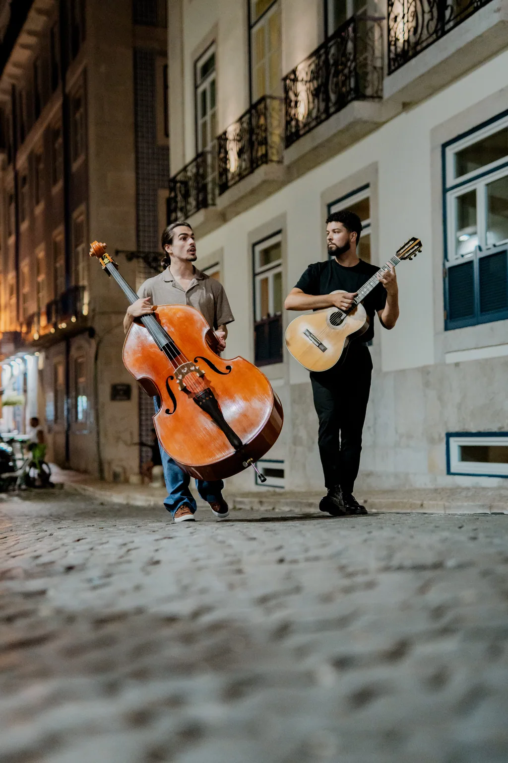 Dois músicos levam o contrabaixo e a viola pela calçada